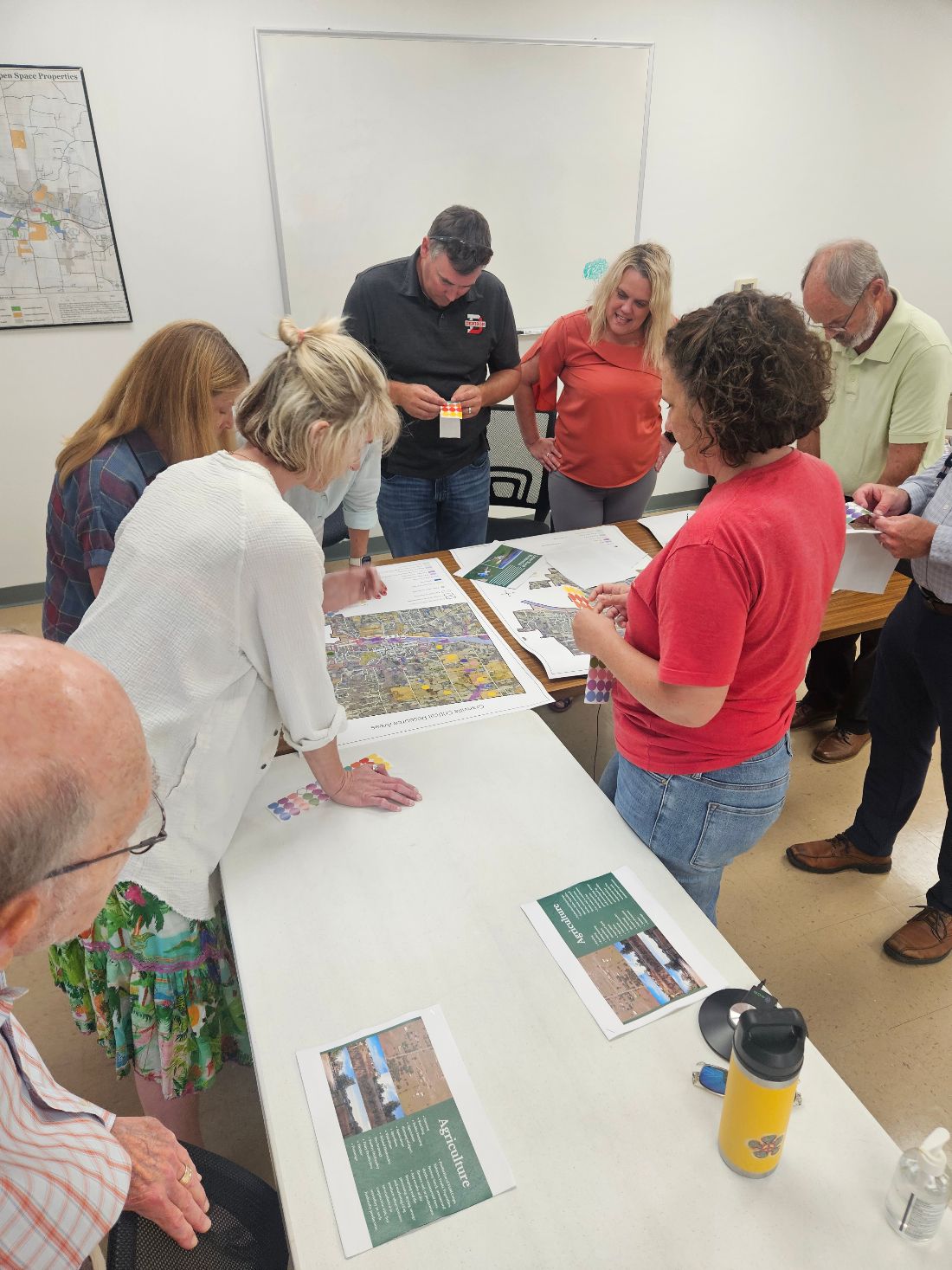 A group gathers around a table of maps and topic boards, placing colored dot stickers