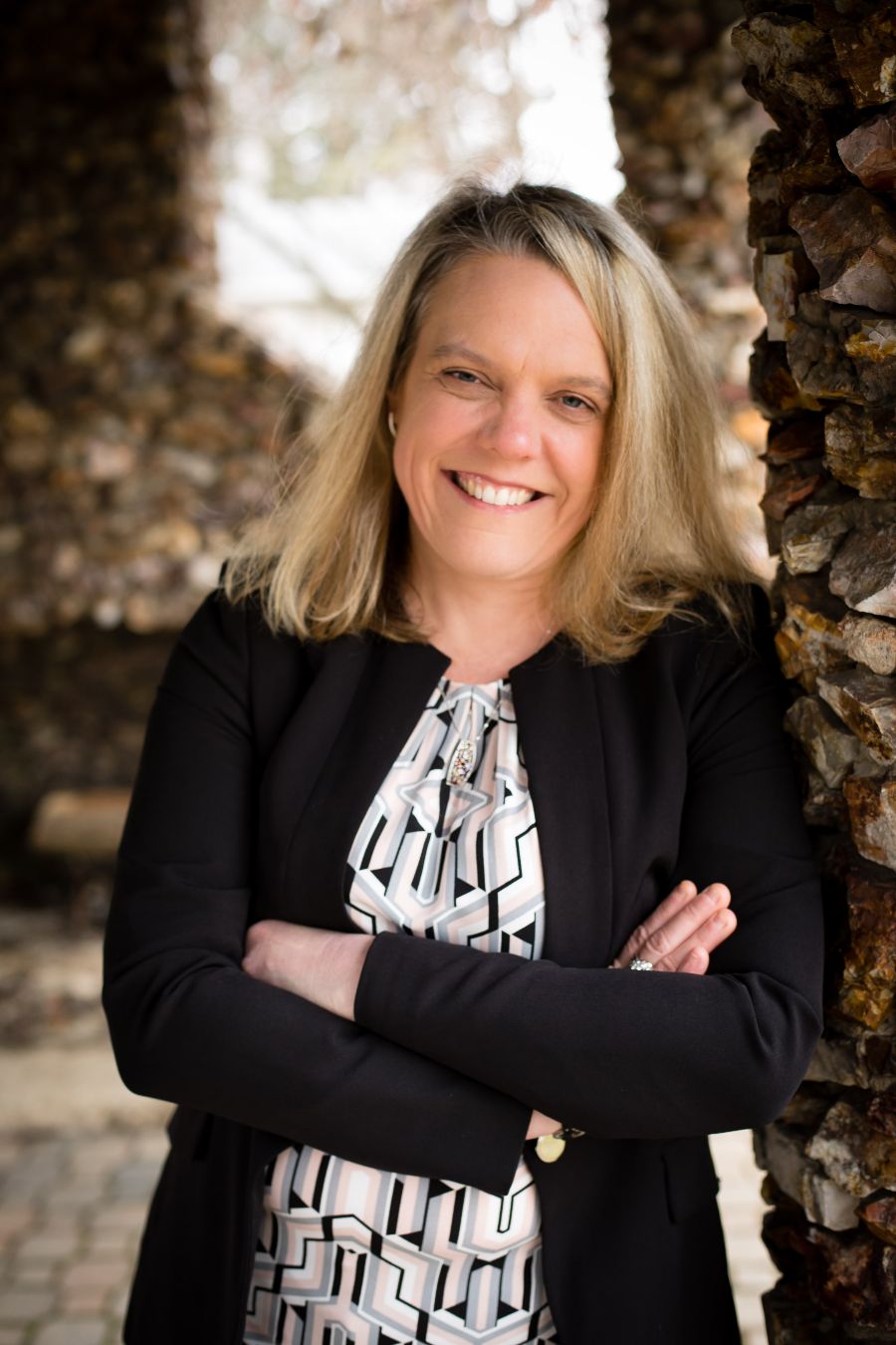 Holly R. Mattei, AICP, smiling with arms crossed beside a stone column